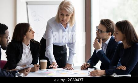 Diverse staff listening serious mature coach provide information during workshop Stock Photo