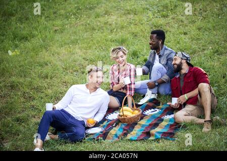 Group of young cheerful coworkers using lunch break time having fun outdoors on green lown, celebrating the start of a new project with fruit drinks Stock Photo