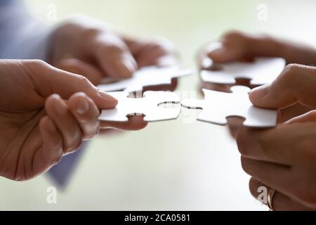 Hands of four businesspeople holding pieces of white puzzles close up Stock Photo