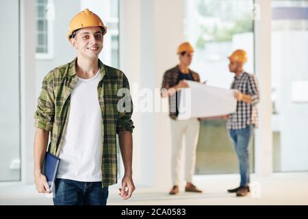 Young smiling middle eastern construction engineer in plaid shirt working on interior finishing with his team Stock Photo
