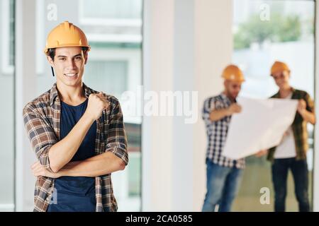 Portrait of handsome young construction engineer with toothy smile standing at construction site and looking at camera Stock Photo