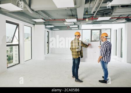 Two young construction engineers discusing blueprint of building and planning works for today Stock Photo