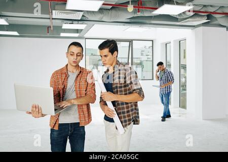 Young architect showing project he was working on to colleague with paper blueprint Stock Photo