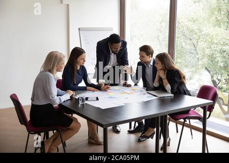 Diverse businesspeople gathered together discussing project financial stats Stock Photo