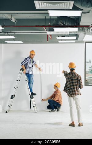 Contractor stepped away to controll workers measuring straight line on wall with measuring tape Stock Photo