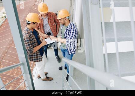 Young builders drinking morning cafe and checking plan of works on tablet computer Stock Photo