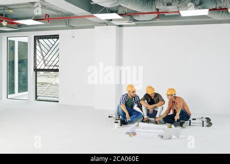 Young construction workers sitting on step ladder with blueprints and color palette in front of them and planning work Stock Photo