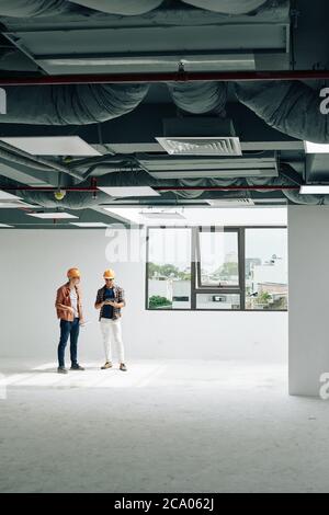 Contractors in hardhats inspecting rooms in empty building after interior finishing works Stock Photo