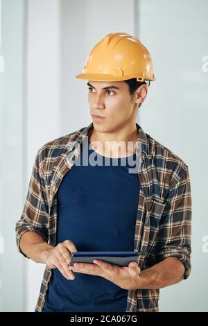 Portrait of serious young civil engineer with digital tablet in hands looking away Stock Photo