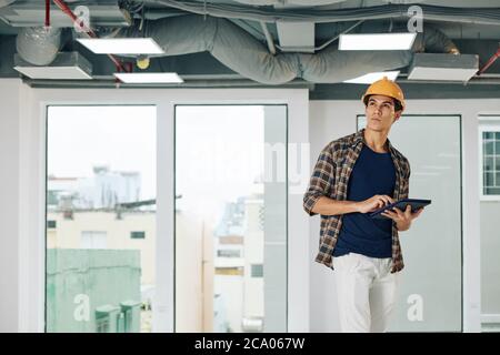 Contractor with digital tablet inspecting house and checking pipes and wires on ceiling Stock Photo