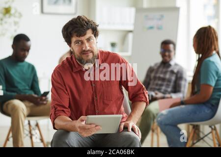 Multi-ethnic group of people sitting in circle while discussing business project in office, focus on mature bearded man looking at camera in foreground, copy space Stock Photo