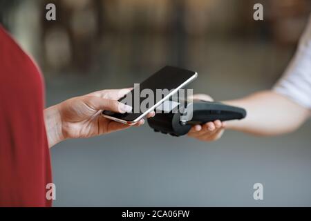 NFC Technology. Unrecognizable woman maiking contactless payment with smartphone to terminal Stock Photo