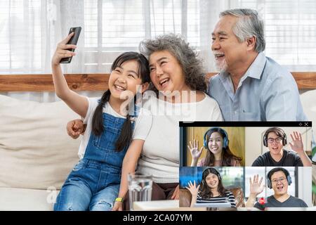 Asian Granddaughter with couple Grandparent taking video call conference to Business people saying hello with teamwork colleague by mobile phone in ho Stock Photo
