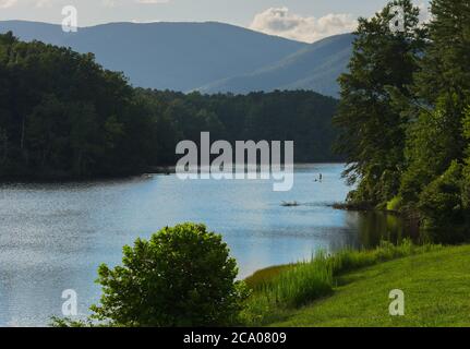 A paddler on a paddleboard enjoys a summer afternoon on a pristine lake in the Blue Ridge Mountains. Stock Photo