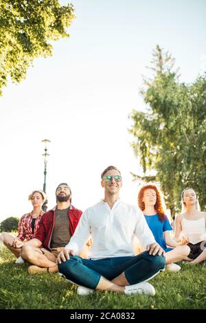 Time for yoga, Attractive young multicultural friends exercising in yoga lotus pose while resting after a long trip in Botanical garden. Multiethnic p Stock Photo