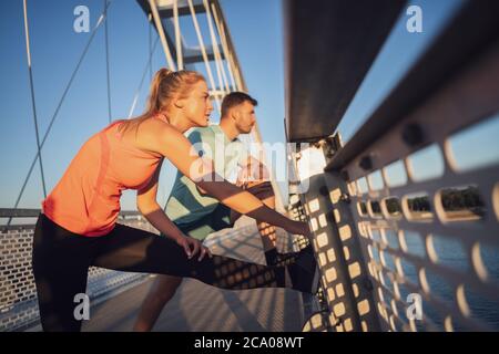Young couple is exercising outdoor on bridge in the city. Stock Photo
