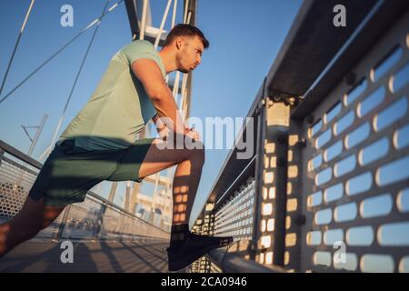 Young man is exercising outdoor on bridge in the city. Stock Photo