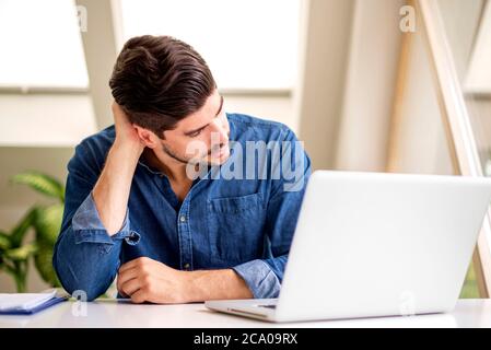Cropped shot of stressed businessman with hand on his neck sitting behind his laptop while having headache. Stock Photo