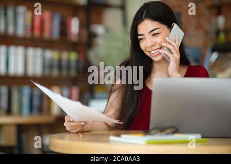 Remote Business. Asian Businesswoman Checking Documents And Talking On Phone In Cafe Stock Photo
