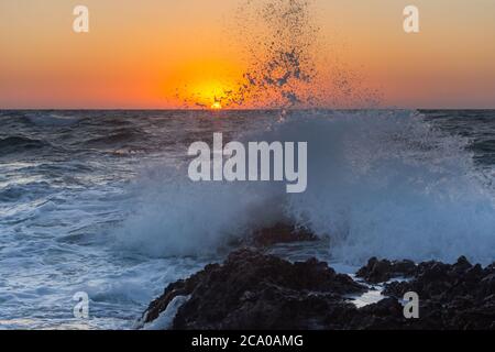 Sunset and storm at sea. Large waves against the background of the setting sun. Summer storm on the Black sea. Beautiful sea spray on the rocks. Stock Photo