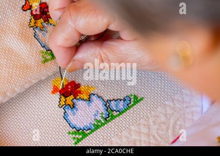 Woman creating black details to a colorful cross stitch design. Concepts of manual work or work at home. Stock Photo