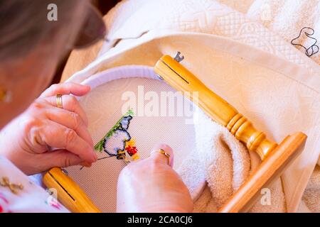 A woman cuts the thread at the back of a cross stitch pattern. Concepts of manual work or work at home. Stock Photo
