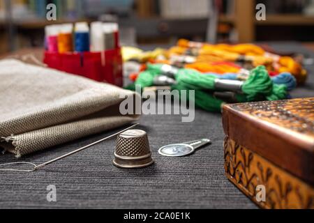 In the foreground a needle lying on a thimble. In the background, fabric and multicolored mouline threads and sewing threads. Stock Photo