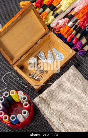 The sewing accessories are in a wooden box. The mulina and colored threads lie on the table next to the casket. The needle with the threaded on it lie Stock Photo