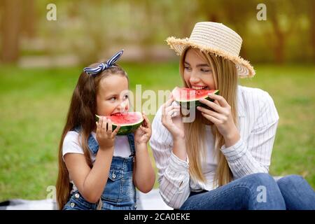 Mother And Daughter Eating Watermelon Sitting On Blanket In Countryside Stock Photo