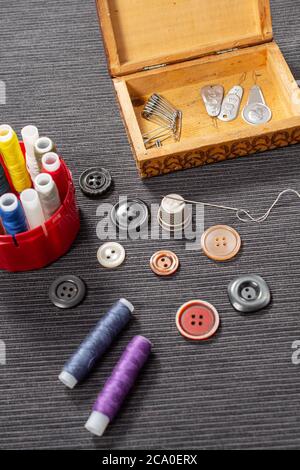 Various colored buttons for clothes lie on the table. Sewing accessories are lying next to you. Sewing a button to clothes. The needle with the thread Stock Photo