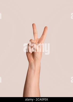 Cropped view of young guy showing victory or peace gesture over light background, close up Stock Photo