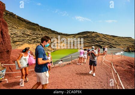 Tourists at Lago Verde (Charco de Los Clicos) viewpoint wear surgical face masks and adhere to social distancing during coronavirus crisis in Spain. Stock Photo