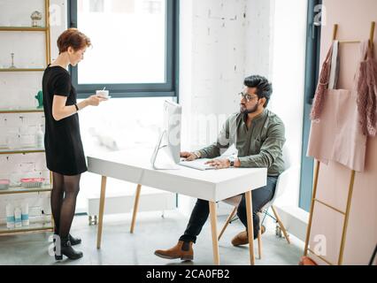 female mentor boss smiling looking at young male coworker and drink coffee, teaching helping colleague Stock Photo
