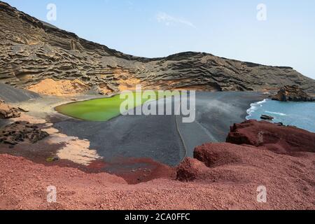 Lago Verde ('Green Lake') in El Golfo, Lanzarote, Canary Islands, Spain. Colorful landscape with black sand beach, dark volcanic rocks and red earth. Stock Photo