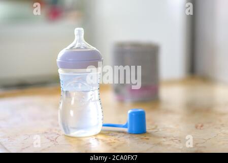 Preparation of mixture baby feeding on marble background in morning kitchen. Feeding bottle with water and baby milk formula with spoon on table.Selective focus. Stock Photo