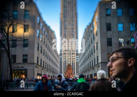 Big Christmas tree stands among the Rockefeller Center buildings under the blue sky. Christmas tree is decorated with 50,000 LED lights and glows in t Stock Photo