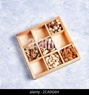 pecans, hazelnuts, almonds, pine nuts, brazil nut, cashews in a wooden box on blue background, top view, flat lay Stock Photo