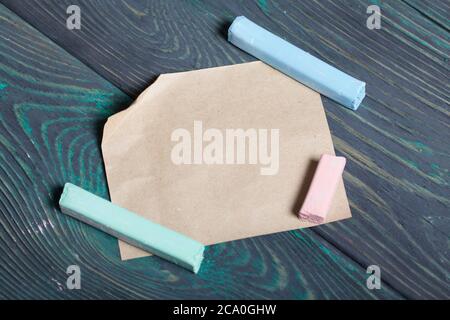 Chalk of different colors and a sheet of paper. On black-green pine planks. Stock Photo