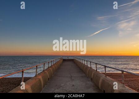 Looking down a jetty out to sea, with a sunset sky behind Stock Photo