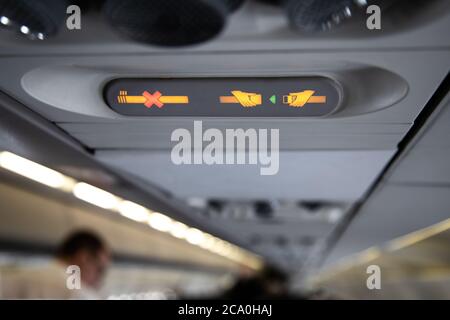 prohibition signs in airplane light up on control panel overhead with signal that shows crossed cigarette and recommendation to buckle up Stock Photo