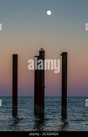 Part of Brighton's West Pier with a sunset behind and a full moon overhead Stock Photo