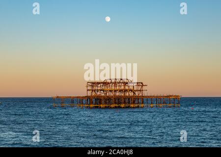 Evening light shining on Brighton's West Pier, with a full moon overhead Stock Photo