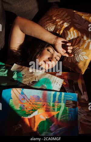 Female artist sleeping on sofa covered with her drawings Stock Photo