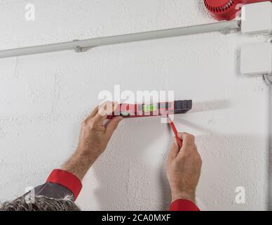 person working with a red spirit level on a white wall, using a red pencil to mark Stock Photo