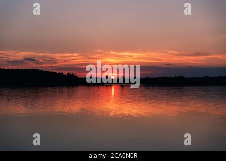 Sun setting behind the trees on horizon of a lake in Ontario, Canada. Stock Photo