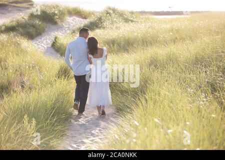 romantic couple from behind walking beach path arm in arm Stock Photo
