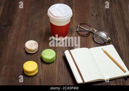 Open notebook with a pencil. Macaroons, paper-cup and a credit card. Wooden background. Top view Stock Photo