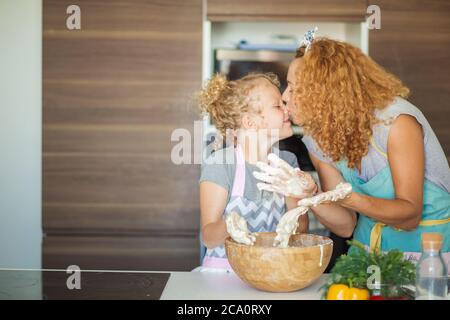 Happy loving caucasian Mom and daughter preparing bakery together, cooking pizza and having fun in the kitchen. Loving couple kissing, hugging with ha Stock Photo