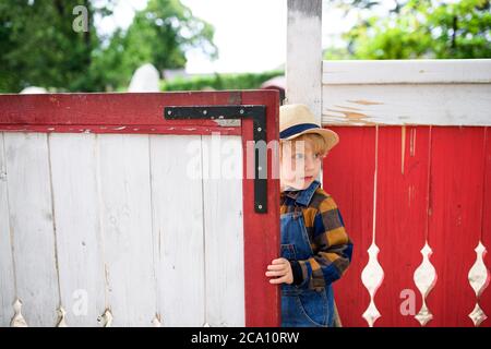 Small boy on farm, opening red and white gate. Stock Photo