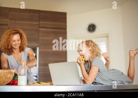 Smiling daughter and mother relaxing on the sofa with notebook while they are looking into the camera Stock Photo
